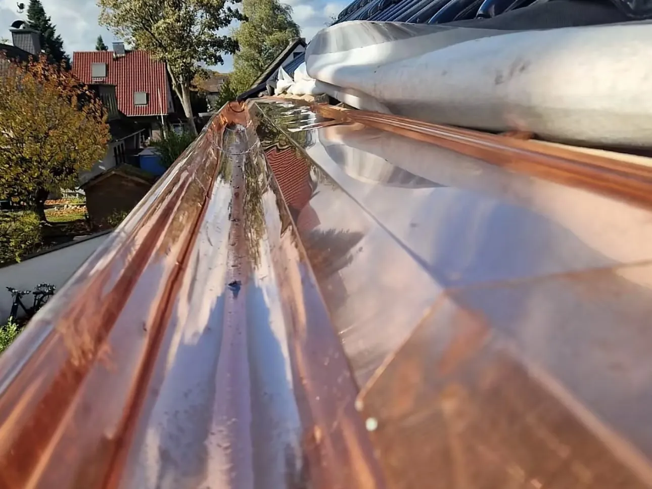 Neu montierte halbrunde Dachrinne aus Kupfer unter glasierten schwarzen Tondachziegeln