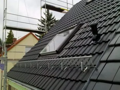 Schneefanggitter und Dachfenster auf einem Dach mit schwarzen Dachziegeln
